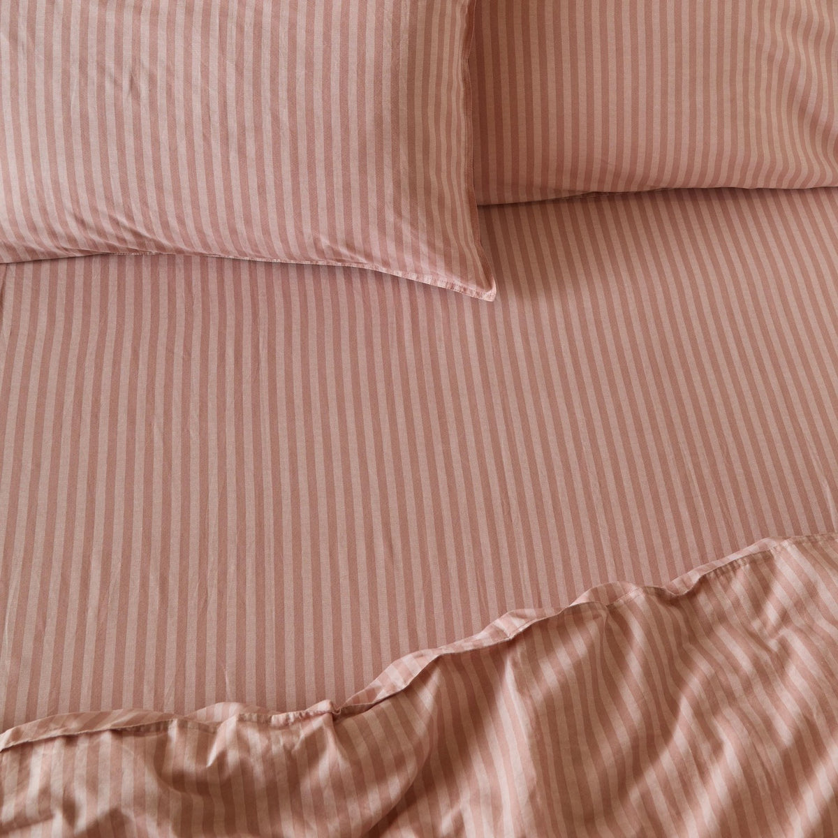 Marlow Stripe cotton fitted sheet in Maple/Sandalwood, shown on a bed with matching pillowcases in a soft dusky pink and lighter stripe pattern.
