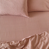 Marlow Stripe cotton fitted sheet in Maple/Sandalwood, shown on a bed with matching pillowcases in a soft dusky pink and lighter stripe pattern.