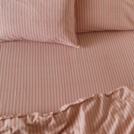 Marlow Stripe cotton fitted sheet in Maple/Sandalwood, shown on a bed with matching pillowcases in a soft dusky pink and lighter stripe pattern.