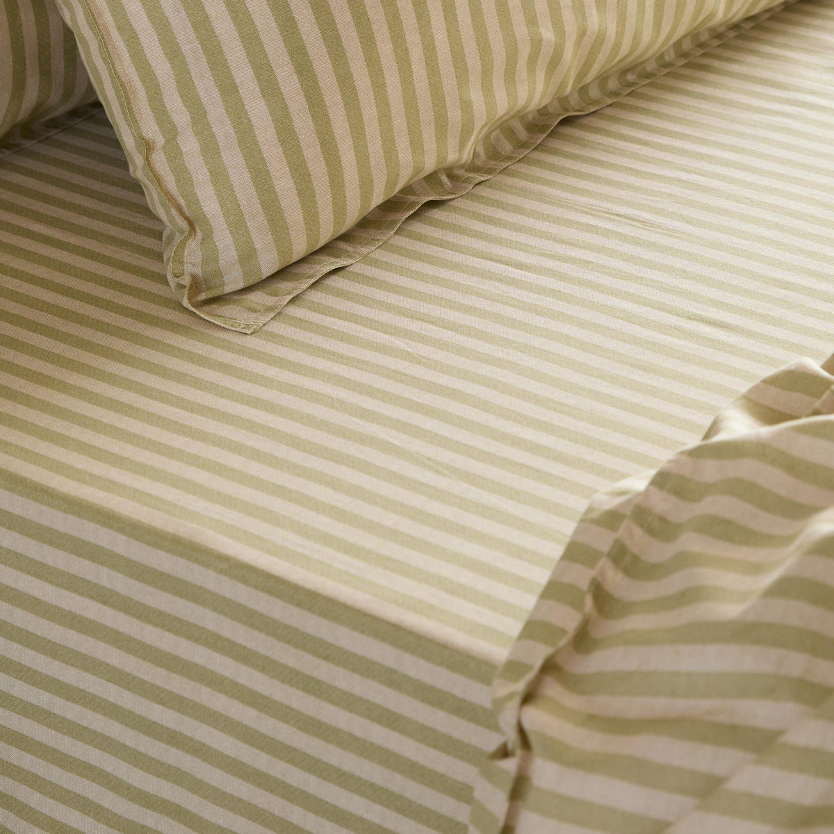 Marlow Stripe Printed Cotton Fitted Sheet in Oregano/Shell, close-up on a bed showing the green and cream striped fitted sheet with matching pillowcase.