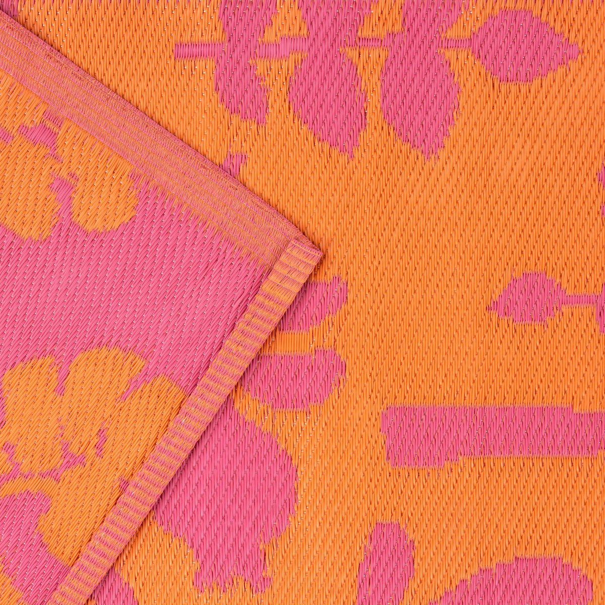 Marula Reversible Jungle Rug in orange and pink, showing folded corner with woven polypropylene texture and tropical leaf pattern on both reversible sides.