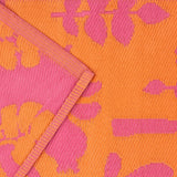 Marula Reversible Jungle Rug in orange and pink, showing folded corner with woven polypropylene texture and tropical leaf pattern on both reversible sides.
