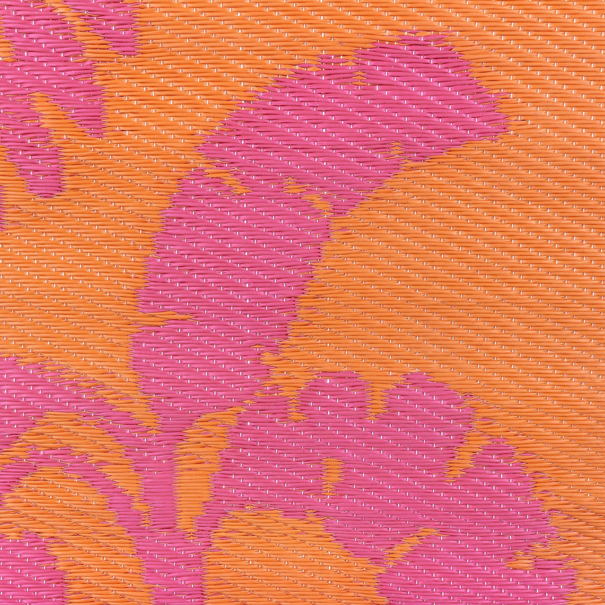 Close-up of the Marula reversible jungle rug's woven polypropylene texture, showing a pink tropical leaf pattern against an orange background.