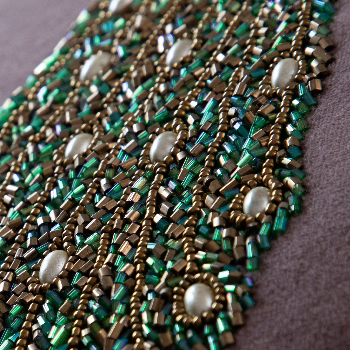Close-up of the Mayura Animal Velvet Cushion showing its beaded peacock tail detail in green, bronze, and pearl-white glass beads with gold embroidery.