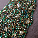 Close-up of the Mayura Animal Velvet Cushion showing its beaded peacock tail detail in green, bronze, and pearl-white glass beads with gold embroidery.