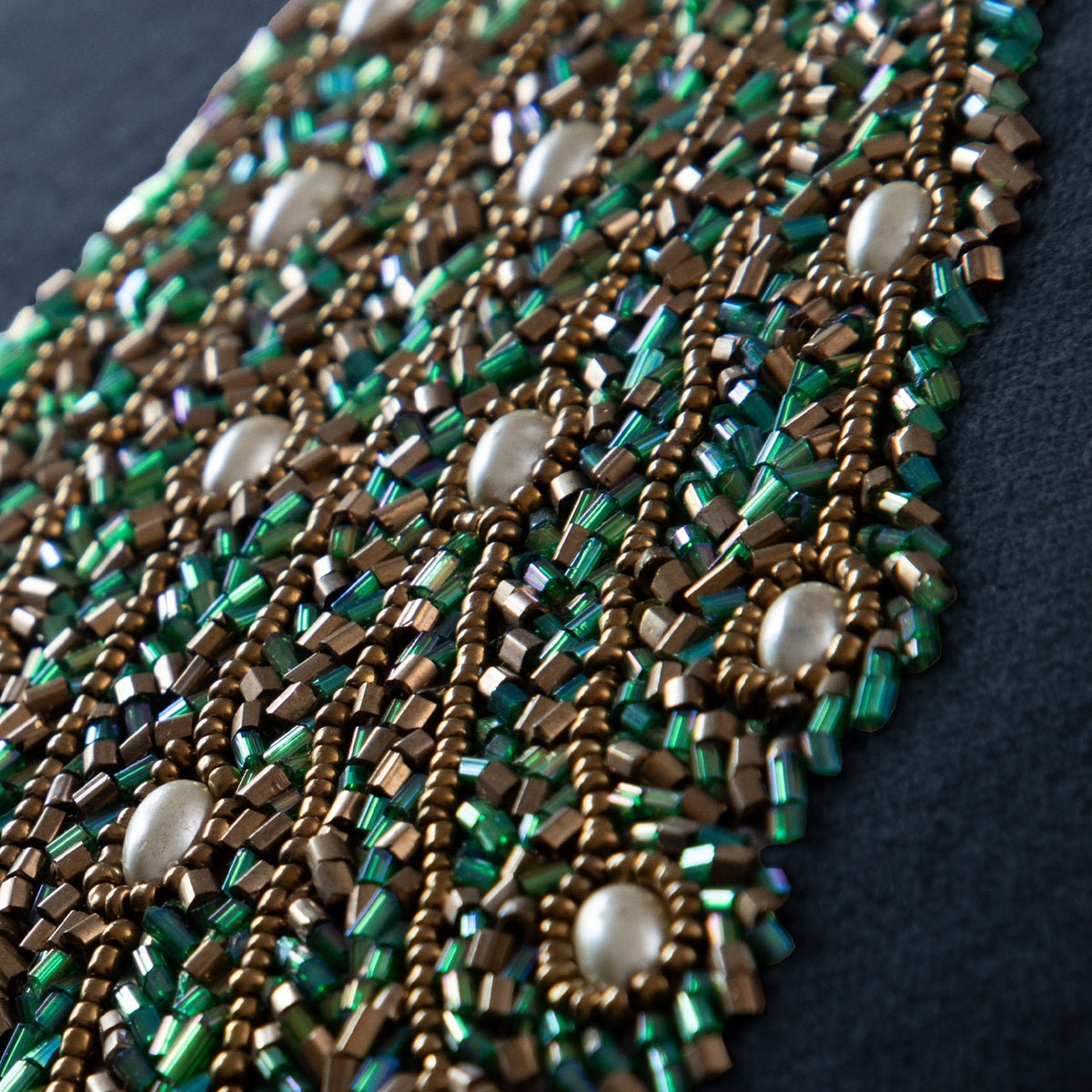 Close-up of the Mayura Animal Velvet Cushion in midnight blue, showing dense green and bronze glass beadwork with pale round beads forming a peacock tail design.