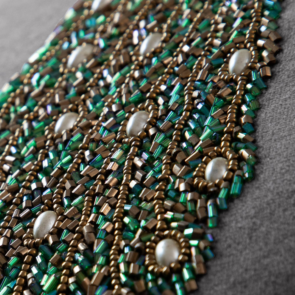 Close-up of the Mayura Animal Velvet Cushion in steel grey, showing hand-beaded peacock tail detail in green and bronze bugle beads with pearl-white cabochons.
