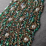 Close-up of the Mayura Animal Velvet Cushion in steel grey, showing hand-beaded peacock tail detail in green and bronze bugle beads with pearl-white cabochons.
