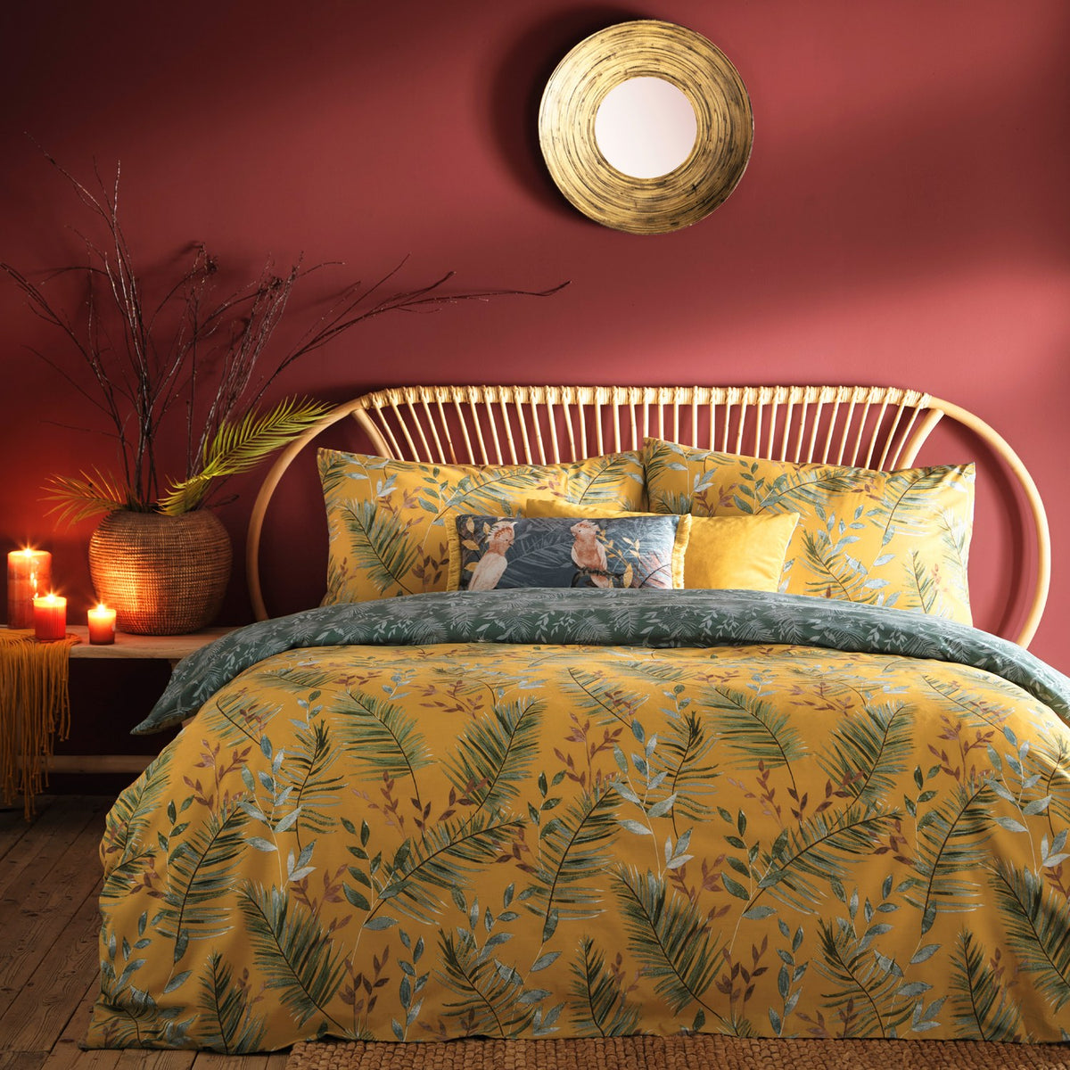 Mazari Printed Jungle Duvet Cover Set in mustard yellow with green palm frond and rust leaf print, styled on a bed with matching pillowcases in a red-walled bedroom.