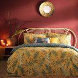 Mazari Printed Jungle Duvet Cover Set in mustard yellow with green palm frond and rust leaf print, styled on a bed with matching pillowcases in a red-walled bedroom.