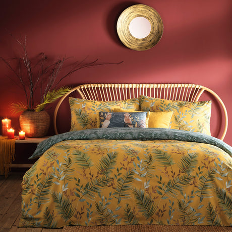 Mazari Printed Jungle Duvet Cover Set in mustard yellow with green palm frond and rust leaf print, styled on a bed with matching pillowcases in a red-walled bedroom.