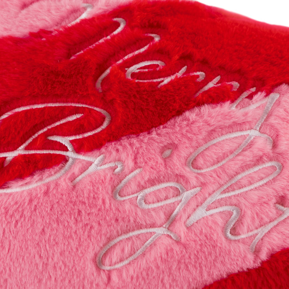 Close-up of the Merry & Bright Striped Faux Fur Cushion in red and pink, showing raised script embroidery on plush diagonal-striped pile fabric.