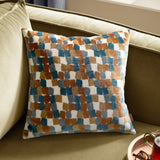 Metro Blocks Jacquard Velvet Cushion in Ginger, featuring a geometric brushstroke pattern in teal, blue, grey and mustard on a cream ground, shown on an olive green sofa.