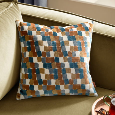 Metro Blocks Jacquard Velvet Cushion in Ginger, featuring a geometric brushstroke pattern in teal, blue, grey and mustard on a cream ground, shown on an olive green sofa.