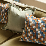 Metro Blocks Jacquard Velvet Cushion in Ginger with geometric cut-velvet blocks in orange, teal, blue and grey on cream, shown on an olive green sofa beside a sage scalloped cushion.