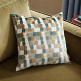 Metro Blocks Jacquard Velvet Cushion in green, featuring an abstract woven block pattern in teal, rust-amber and ochre on cream, shown on a green sofa.