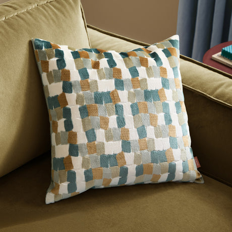 Metro Blocks Jacquard Velvet Cushion in green, featuring an abstract woven block pattern in teal, rust-amber and ochre on cream, shown on a green sofa.