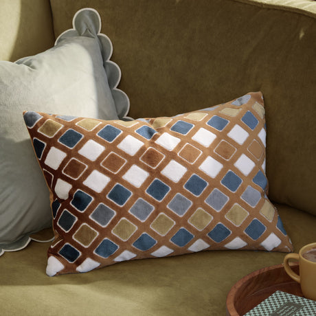 Metro Diamond Jacquard Velvet Cushion in gold and blue, rectangular with a rust-toned diamond pattern, shown on an olive-green sofa beside a scalloped grey pillow.