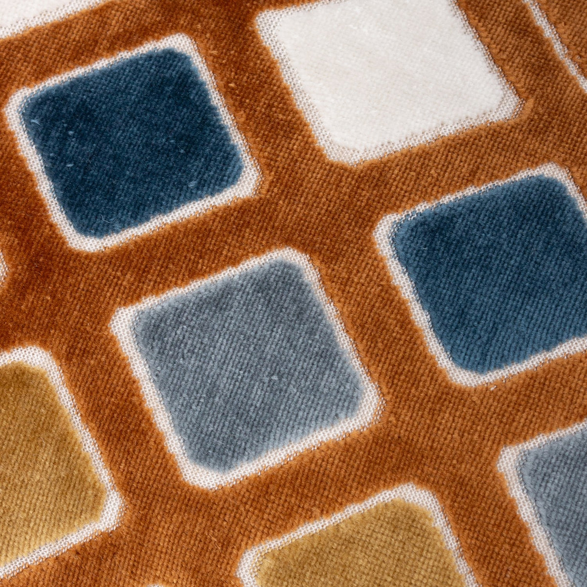 Close-up of the Metro Diamond Jacquard Velvet Cushion showing raised velvet diamond shapes in teal, dusty blue, gold and cream set within a rust-orange grid pattern.