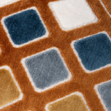 Close-up of the Metro Diamond Jacquard Velvet Cushion showing raised velvet diamond shapes in teal, dusty blue, gold and cream set within a rust-orange grid pattern.