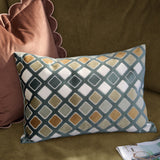 Metro Diamond Jacquard Velvet Cushion in green, rectangular with a diagonal diamond pattern in teal, orange, sage and cream, shown on a green sofa beside a pink cushion.