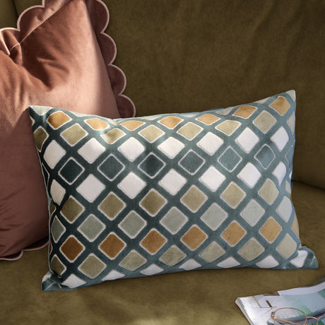 Metro Diamond Jacquard Velvet Cushion in green, rectangular with a diagonal diamond pattern in teal, orange, sage and cream, shown on a green sofa beside a pink cushion.