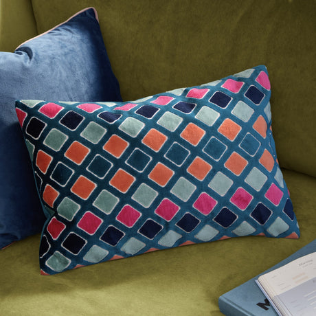 Rectangular Metro Diamond cushion in jacquard velvet, teal ground with pink, orange, navy and sage diamond pattern, shown on an olive green sofa beside a blue velvet cushion.