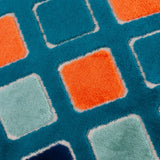 Close-up of the Metro Diamond Jacquard Velvet Cushion, showing a teal ground with a diamond grid pattern in orange, sage, and navy velvet squares outlined in cream stitching.