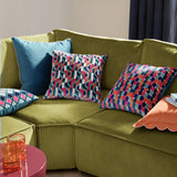 Metro Diamond jacquard velvet cushion in a multicoloured diamond grid pattern with teal, pink, orange and navy tones, styled on an olive green sofa alongside patterned and plain teal cushions.