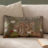 Rectangular sage green chenille cushion with printed hare and wildflower design, styled on a beige sofa beside a textured cream cushion.
