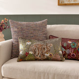Meadow Bloom Animal Chenille Cushion in sage, a rectangular bolster printed with a hare among wildflowers, styled on a beige sofa with patterned and floral cushions.