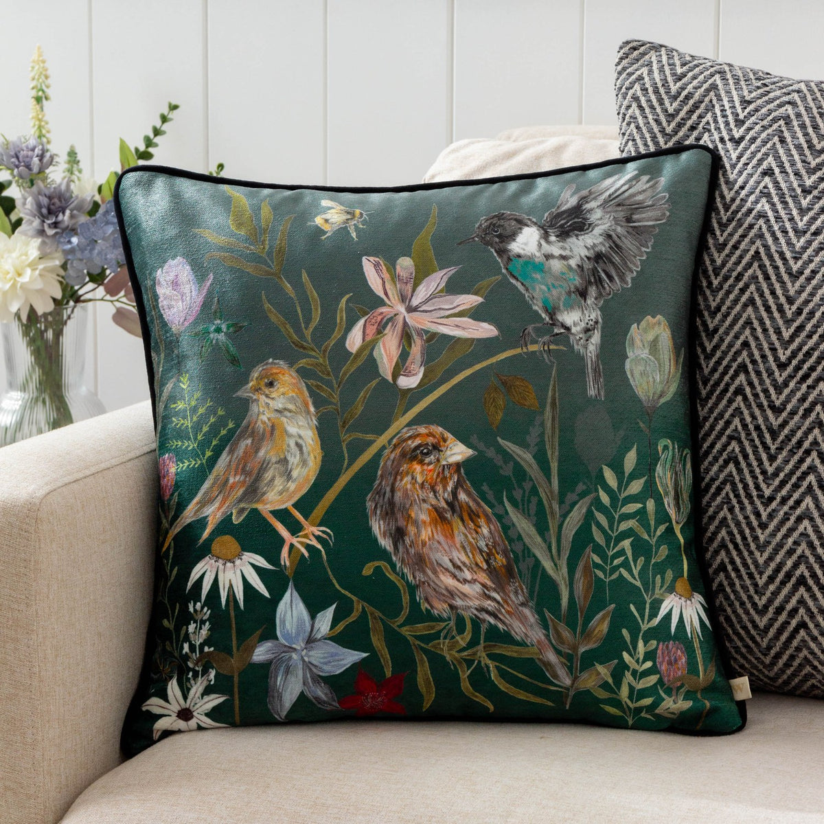 Meadow Bloom Animal Chenille Cushion in teal, showing hand-painted birds and wildflowers on a deep green square cushion, styled on a living room sofa.