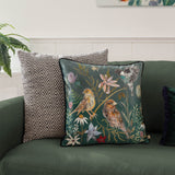 Meadow Bloom Animal Chenille Cushion in teal, printed with hand-painted birds, wildflowers and foliage, shown on a green sofa beside a chevron-patterned cushion.