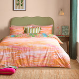 Meadow Escape reversible duvet cover set on a bed with green upholstered headboard, showing the peach and pink abstract side with a floral-print pillowcase edge visible.