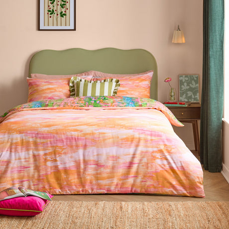 Meadow Escape reversible duvet cover set on a bed with green upholstered headboard, showing the peach and pink abstract side with a floral-print pillowcase edge visible.