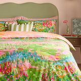 Meadow Escape reversible duvet cover set on a bed with green upholstered headboard, showing the painterly wildflower meadow print in green, pink, orange and blue tones.