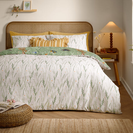 Reversible Meadow Flora Duvet Cover Set shown reverse side up, white ground with green grass stem print, styled with striped and ruffled cushions in a rattan-headboard bedroom.