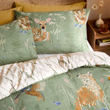 Meadow Flora Reversible Animal Duvet Cover Set in green, styled on a bed with pillowcases showing a fox and deer in floral pattern, reverse side in pale grass-stem print, in a bedroom setting.