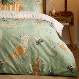 Meadow Flora Reversible Animal Duvet Cover Set in green, shown on a bed with woodland motifs of a fox, rabbits, kingfisher and bees, styled in a bedroom with a wooden side table.