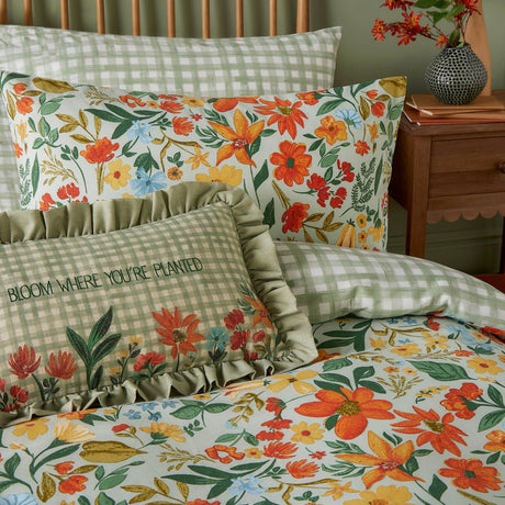 Meadow Haze Reversible Gingham Duvet Cover Set in green styled on a bed with matching pillowcases, a ruffled cushion reading "Bloom Where You're Planted", and a wildflower print bolster.