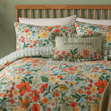 Meadow Haze reversible duvet cover set on a bed, wildflower floral print in orange, yellow and green on pale ground, with matching pillowcases and a green gingham reverse edge visible.