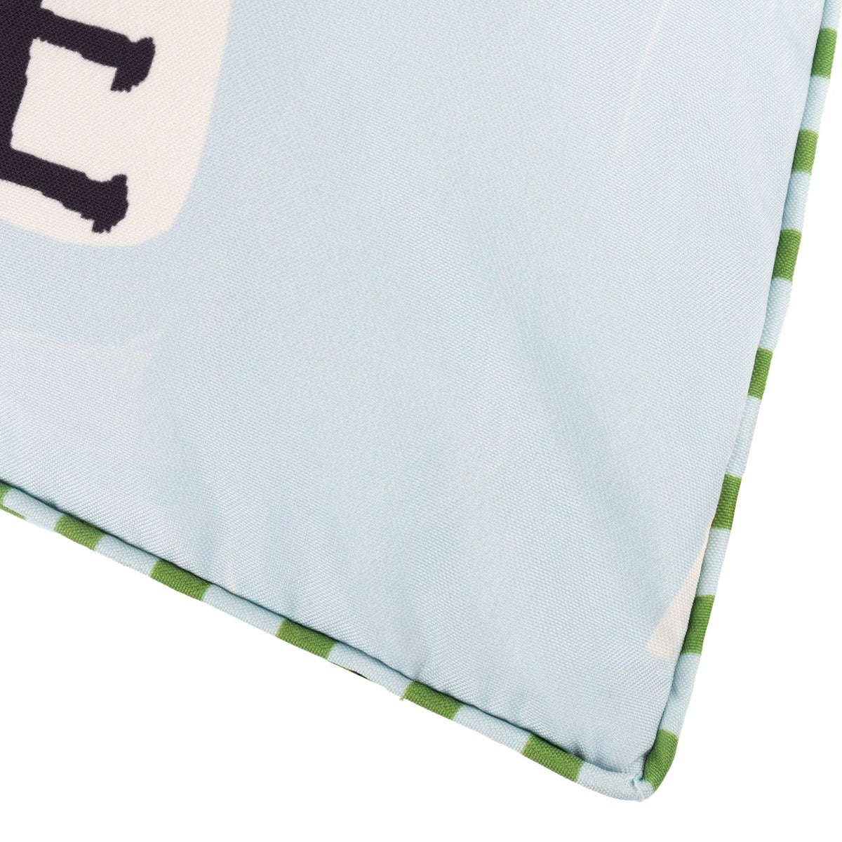 Close-up of the Mediterranean Olive reversible polyester cushion corner, showing pale sky-blue fabric with black lettering and green striped piped trim edging.