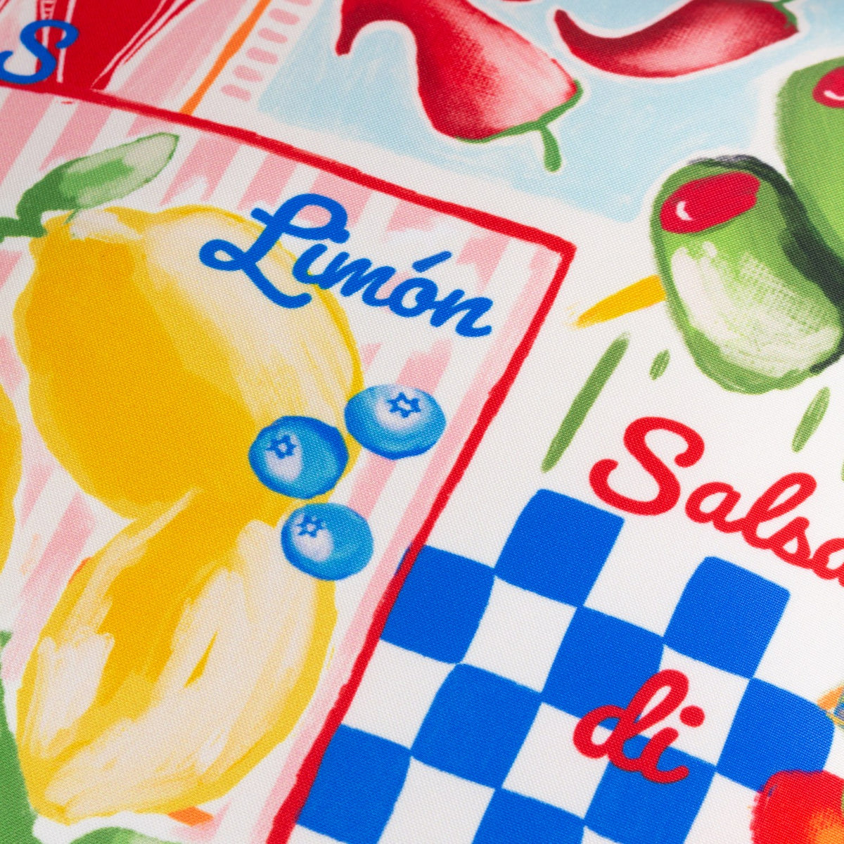 Close-up of the Mediterranean Picnic Abstract Polyester Cushion, showing hand-painted lemons, blueberries and olives with "Limón" text on pink stripes and blue gingham panels.