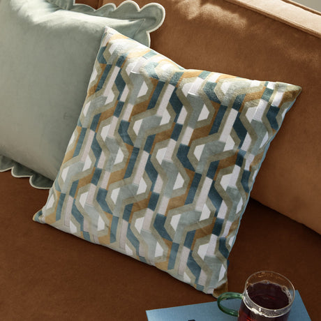 Metro Prism Jacquard Velvet Cushion in green, a 45x45cm square cushion with an interlocking geometric pattern in teal, ochre, sage and cream, shown styled on a tan sofa.