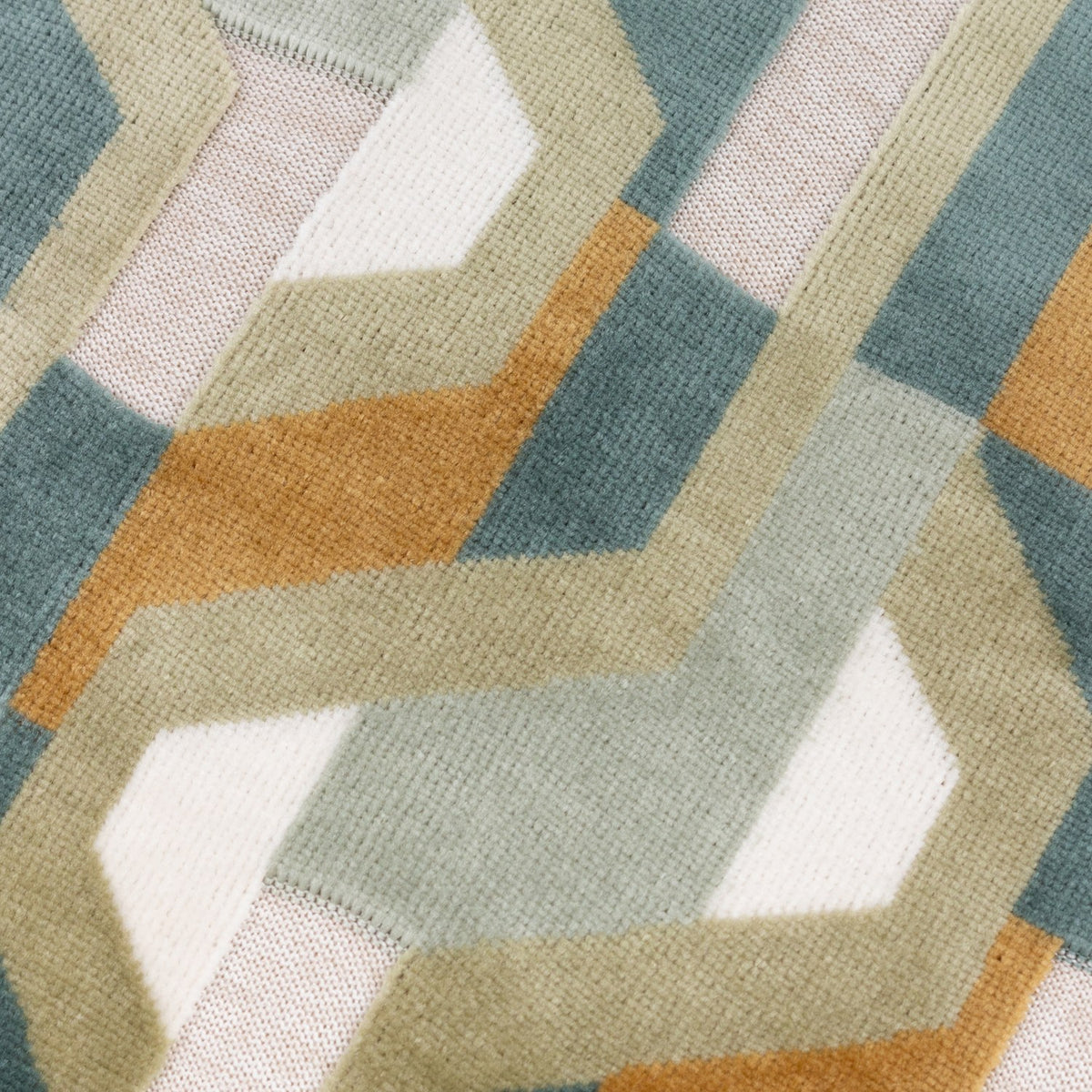 Close-up of the Metro Prism cushion's velvet jacquard face, showing an angular geometric pattern woven in teal, ochre, sage, soft grey and cream.