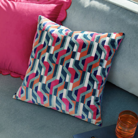 Metro Prism Jacquard Velvet Cushion in pink, orange, teal, navy and cream, showing a textured geometric pattern, styled on a grey sofa beside a pink velvet cushion.