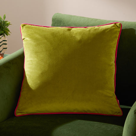 Meridian Plain Velvet Cushion in lime green with contrasting hot pink piped border, shown on a green velvet sofa in a living room setting.