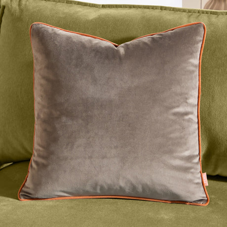 Meridian Plain Velvet Cushion in mocha brown with contrasting pumpkin orange piped edge, shown square-shaped on a green sofa.