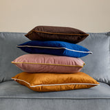 Meridian Plain Velvet Cushion in navy blue with silver-grey piped edge, shown velvet-textured and stacked with other cushions on a grey sofa.