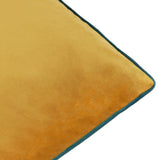 Close-up of the Meridian Plain Velvet Cushion in ochre, showing soft-touch velvet texture and teal piped edge trim against a white background.